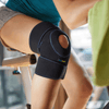 Lifestyle image of woman wearing the Actimove Sport Knee Support Open Patella Adjustable Universal while exercising on a stationary bike indoors. Confidently work out, run or cycle, as this sleeve doesn't overly restrict movement.