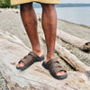 Front view of man wearing the Brown Hatcher sandal outside while standing on a log from the knees down.