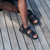 Top-down view of man wearing Black Propet men's sandals with legs crossed while sitting on ground outside