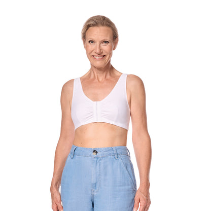 A smiling older woman wearing a white bra with a gathered center front, paired with light blue jeans, photographed against a solid white background.
