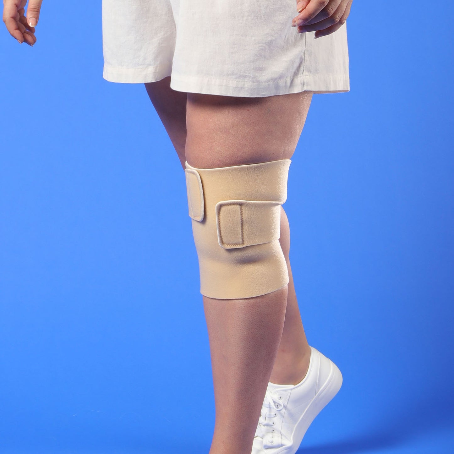 Person wearing a beige Thuasne Biflex Self Adjust wrap knee against a blue background
