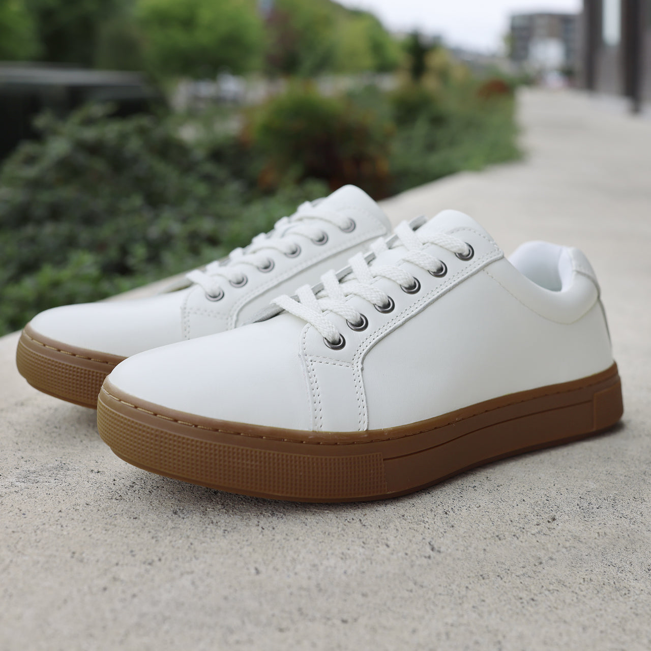 Propet Koda Men's Platform Sneaker White sneakers with brown soles on a concrete surface with greenery in the background