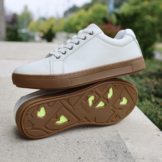 Propet Koda Men's Platform Sneaker - Propet Koda Men's Platform Sneaker White sneakers with brown soles on a concrete surface with greenery in the background