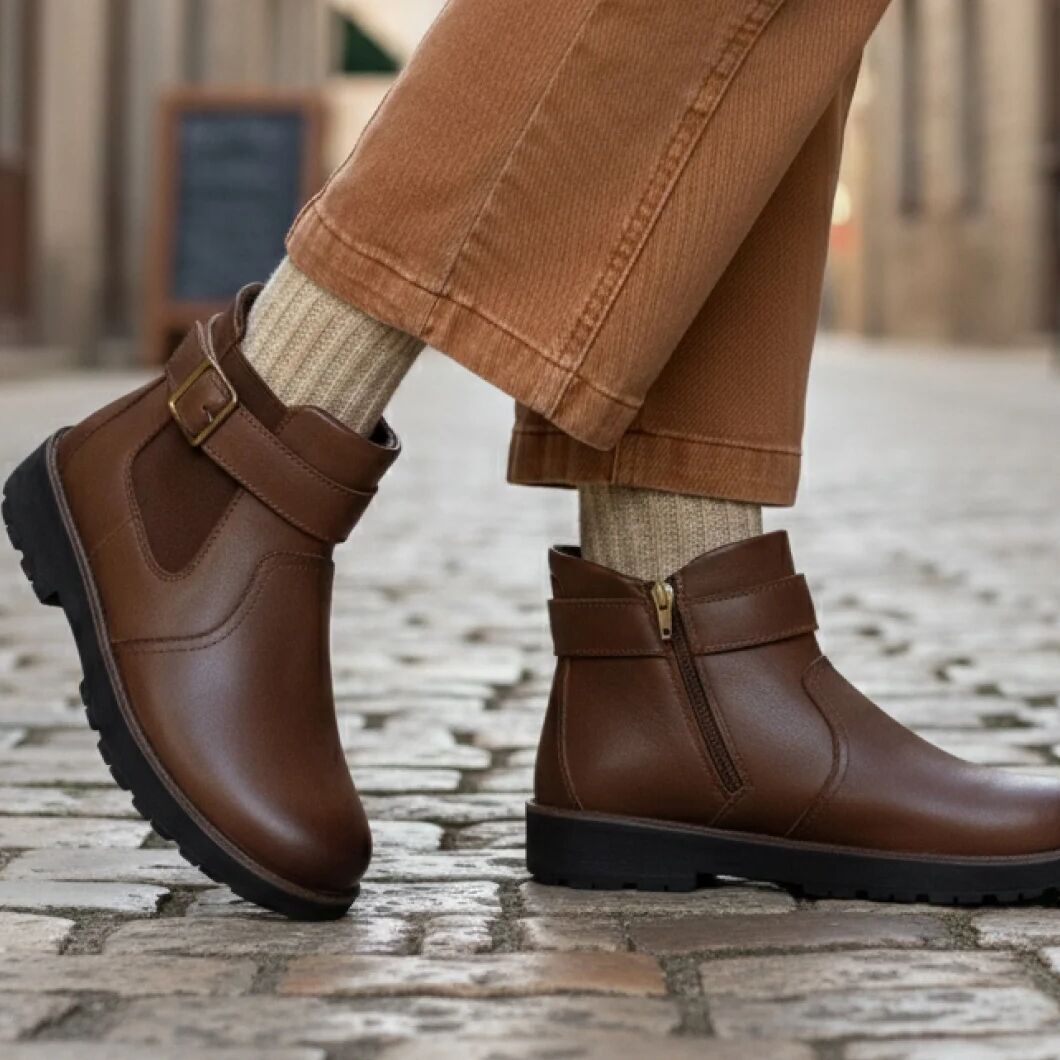 Brown leather boots worn with beige pants and socks on a stone pavement.