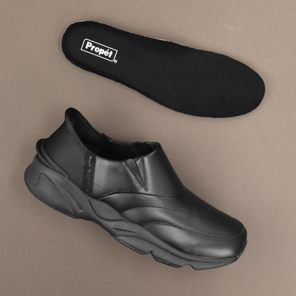 A black slip-on shoe shown from the side with its matching black insole placed above it on a plain taupe background. The insole has a visible white 'Propél' logo.
