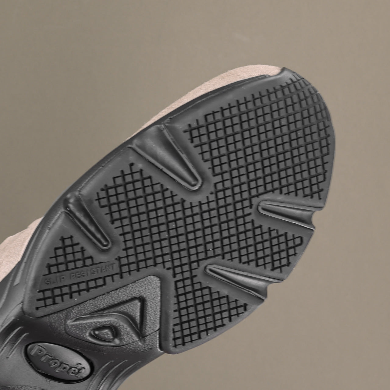Close-up of the textured black outsole of a sneaker, showing the Propát logo and grip pattern, against a solid taupe background.