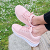 a person's feet on a wooden surface wearing Pink Ultima X walking shoes with feet crossed
